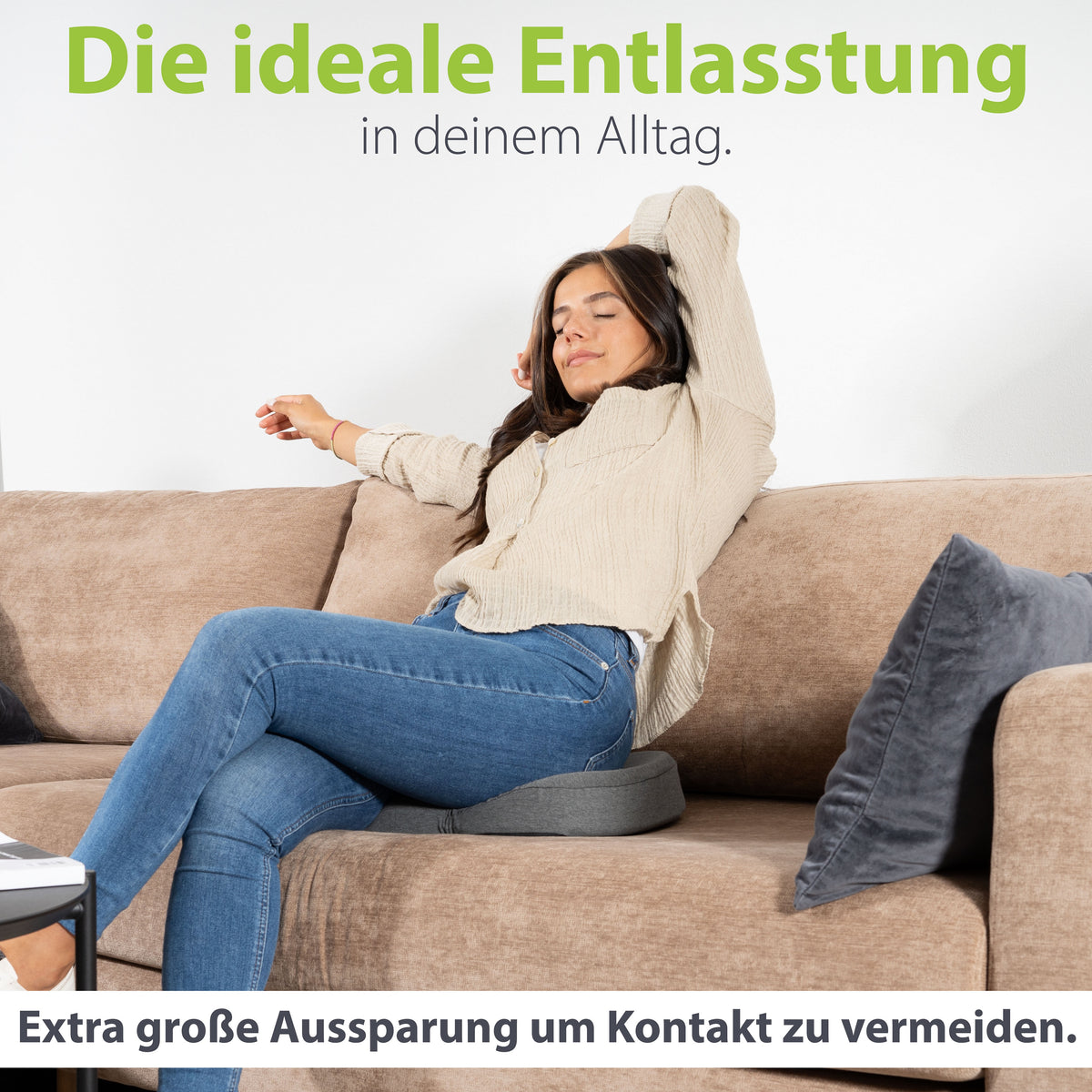 Frau entspannt auf dem Sofa mit erhobenen Armen, sitzend auf einem ergonomischen Kissen von feela, das durch seine extra große Aussparung Druckkontakt vermeidet.